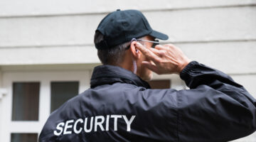 Security Guard Listening To Earpiece Against Building